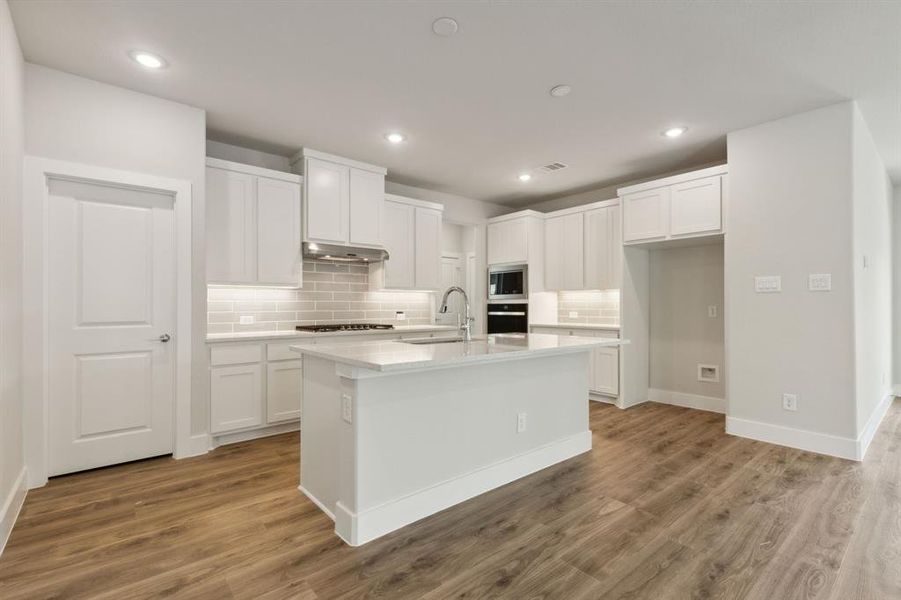 Kitchen featuring light wood-type flooring, white cabinetry, a kitchen island with sink, and sink