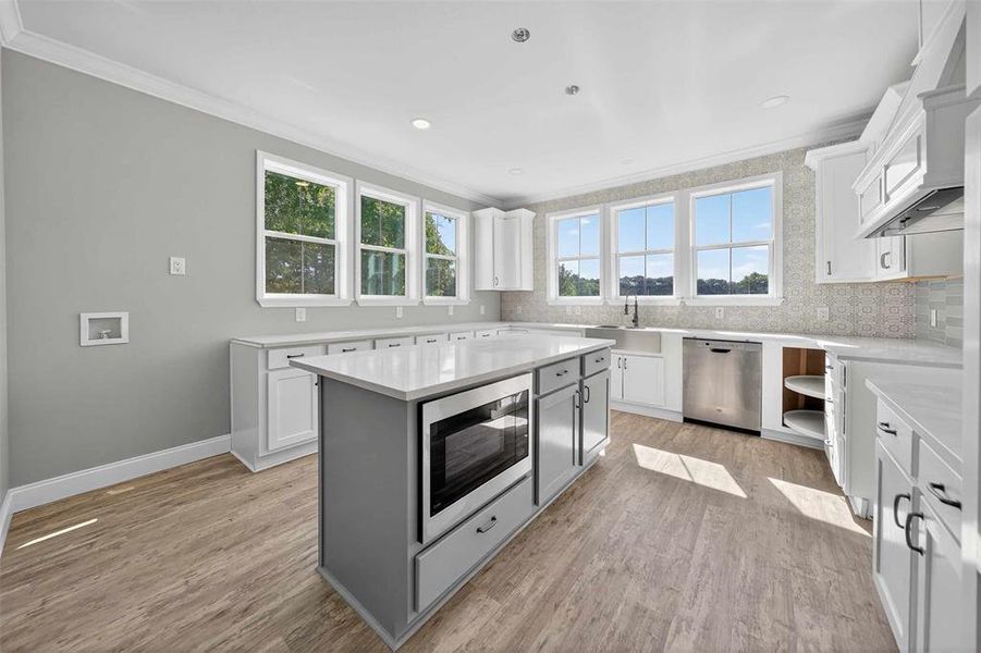 Kitchen featuring backsplash, stainless steel appliances, ornamental molding, light wood-style floors, and white cabinetry