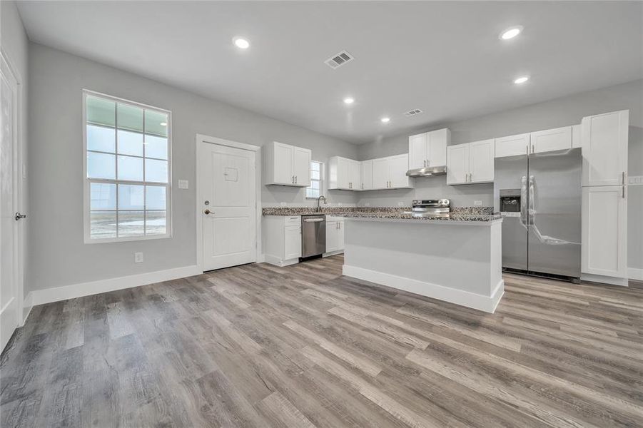 Kitchen with stainless steel appliances, a kitchen island, white cabinets, and light hardwood / wood-style floors