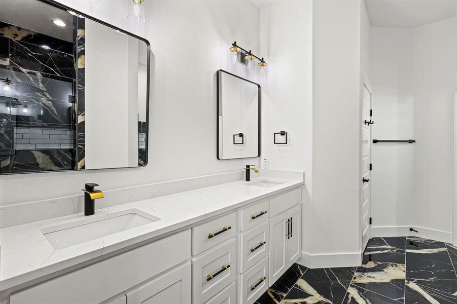 Full bath with marble finish floor, double vanity, a sink, and baseboards