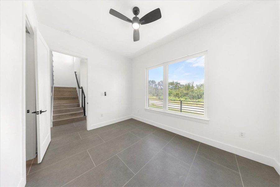 Empty room featuring stairway, a ceiling fan, and dark tile patterned flooring Empty room featuring stairway, a ceiling fan, and dark tile patterned flooring