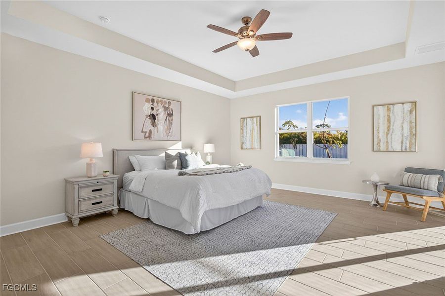 Bedroom with a tray ceiling, wood tiled floors, and ceiling fan