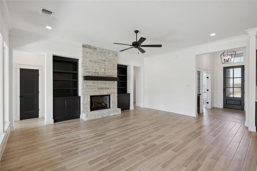 Unfurnished living room with ceiling fan with notable chandelier, light hardwood / wood-style floors, built in shelves, ornamental molding, and a brick fireplace