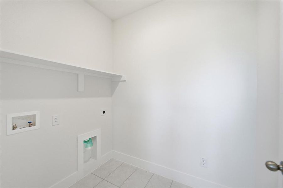Dedicated laundry area featuring a white storage shelf, utility hookups, and light-toned tile flooring