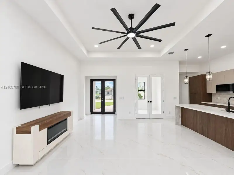 Tray ceiling with a multi-blade matte black ceiling fan, polished stone-finish flooring, two-tone custom cabinetry, stone-surface kitchen island, and built-in electric fireplace