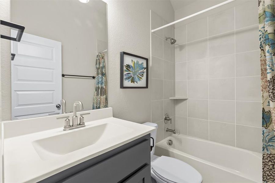 Bathroom featuring toilet, a textured wall, shower / bath combo, and vanity