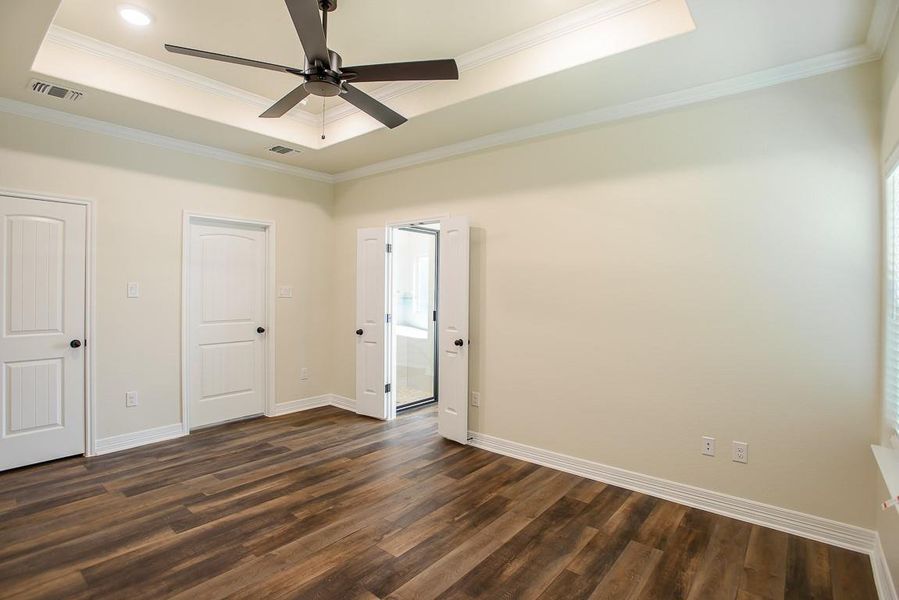 Unfurnished bedroom featuring a raised ceiling, dark wood-type flooring, crown molding, and a ceiling fan Unfurnished bedroom featuring a raised ceiling, dark wood-type flooring, crown molding, and a ceiling fan