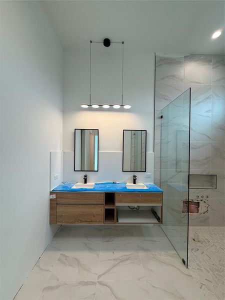 Full bath featuring a marble finish shower, double vanity, and marble look tile flooring Full bath featuring a marble finish shower, double vanity, and marble look tile flooring