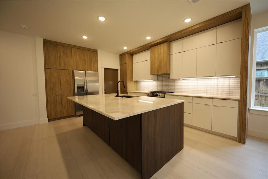 Kitchen featuring modern cabinets, decorative backsplash, light stone countertops, an island with sink, and recessed lighting