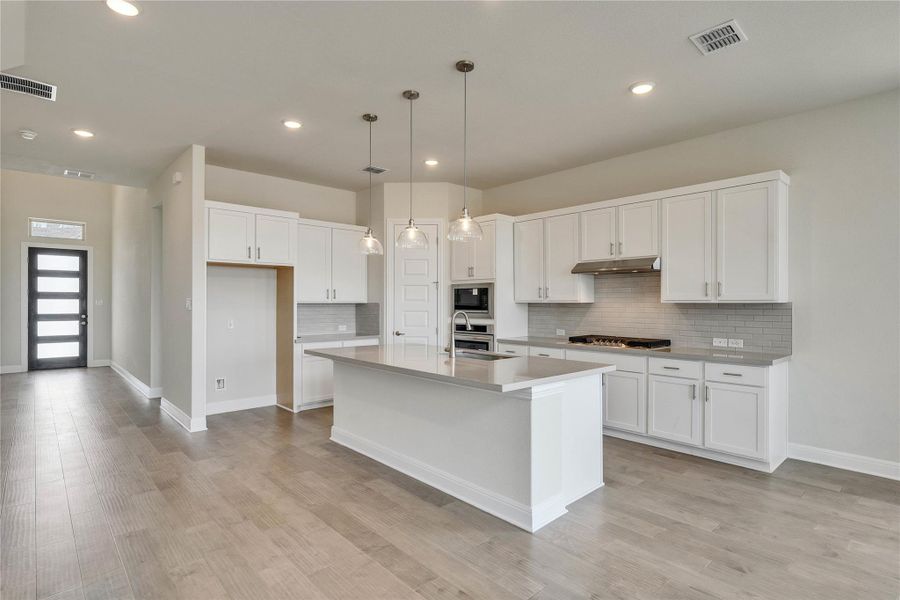 Kitchen with decorative backsplash, a kitchen island with sink, white cabinets, light wood-style floors, and light countertops Kitchen with decorative backsplash, a kitchen island with sink, white cabinets, light wood-style floors, and light countertops