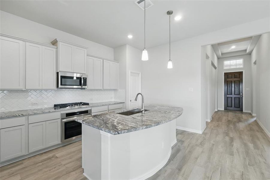 Kitchen featuring stainless steel appliances, light stone countertops, a center island with sink, and light wood-style floors Kitchen featuring stainless steel appliances, light stone countertops, a center island with sink, and light wood-style floors