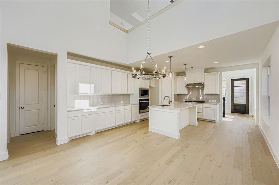 Kitchen with decorative backsplash, white cabinets, light wood-style floors, a chandelier, and decorative light fixtures