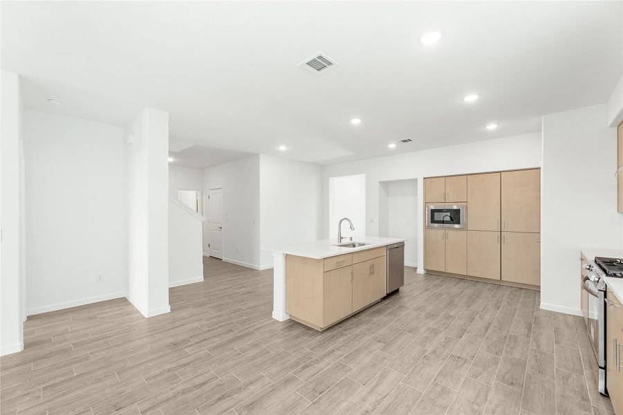 Open kitchen with light wood cabinets, center island with sink, and wood-look tile floors