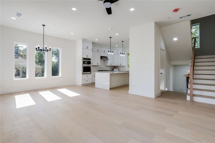 Unfurnished living room with healthy amount of natural light, recessed lighting, a chandelier, light wood-style flooring, and stairway