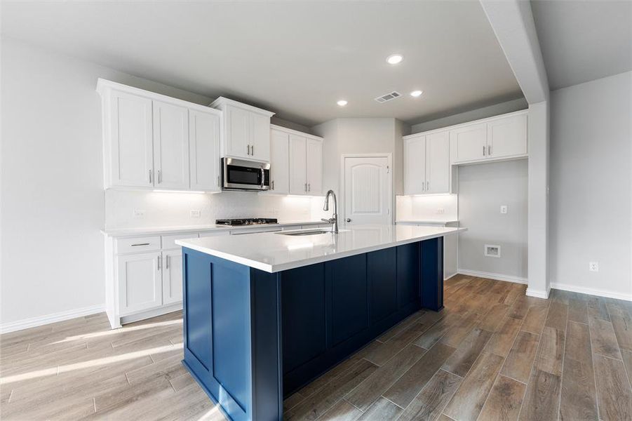 Kitchen with white cabinetry, wood tiled floors, an island with sink, recessed lighting, and stainless steel microwave