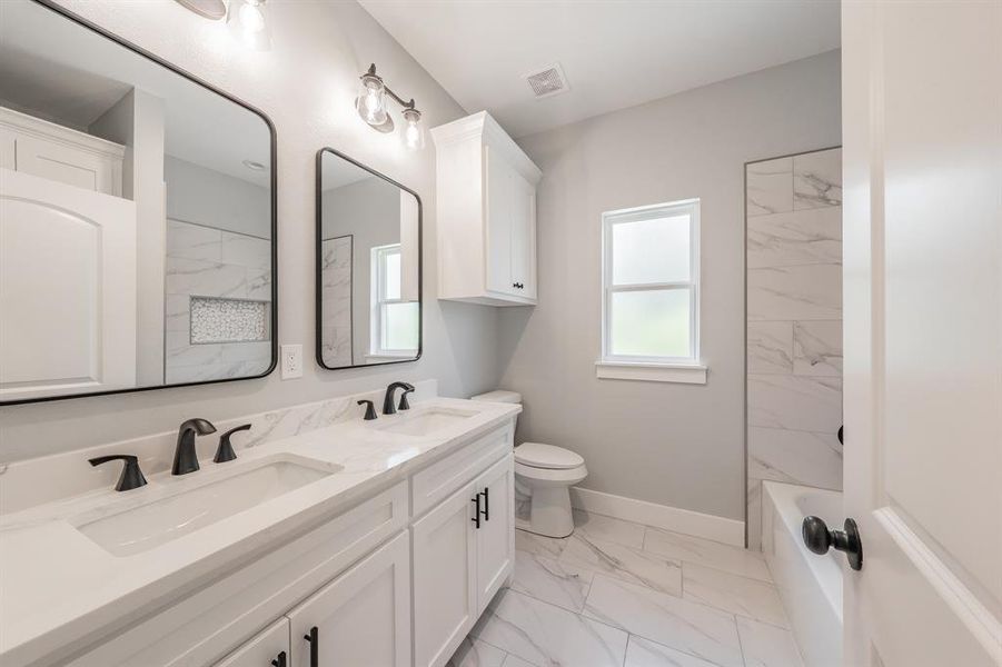 Full bathroom featuring double sink vanity, toilet, tile patterned flooring, and tiled shower / bath