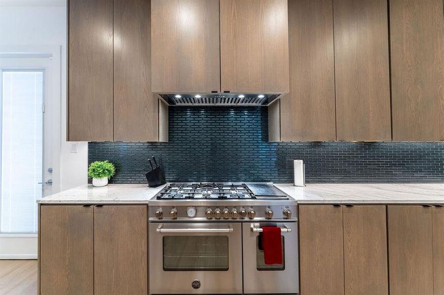 Kitchen with backsplash, double oven range, light hardwood / wood-style floors, and light stone countertops Kitchen with backsplash, double oven range, light hardwood / wood-style floors, and light stone countertops