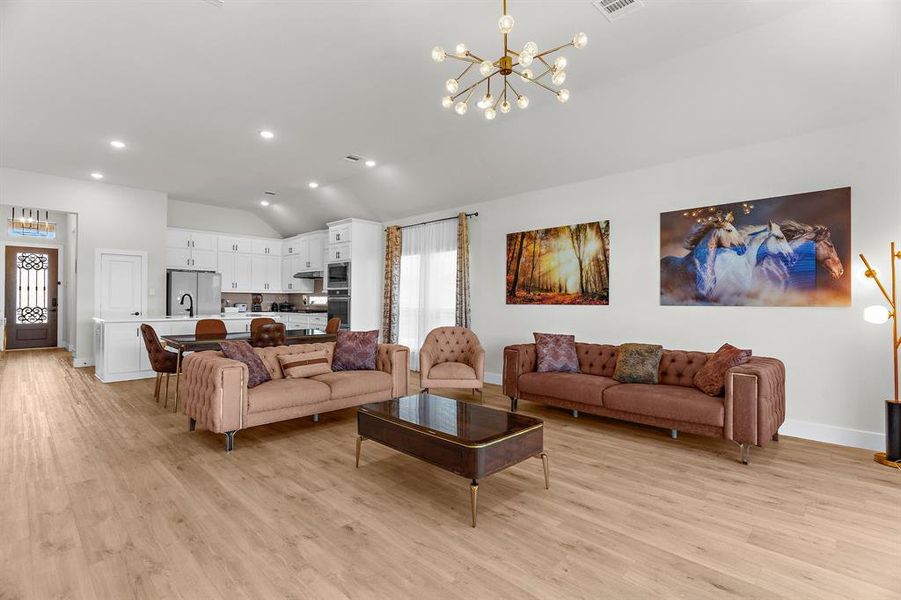 Living room with a chandelier, vaulted ceiling, light wood-type flooring, recessed lighting, and baseboards Living room with a chandelier, vaulted ceiling, light wood-type flooring, recessed lighting, and baseboards