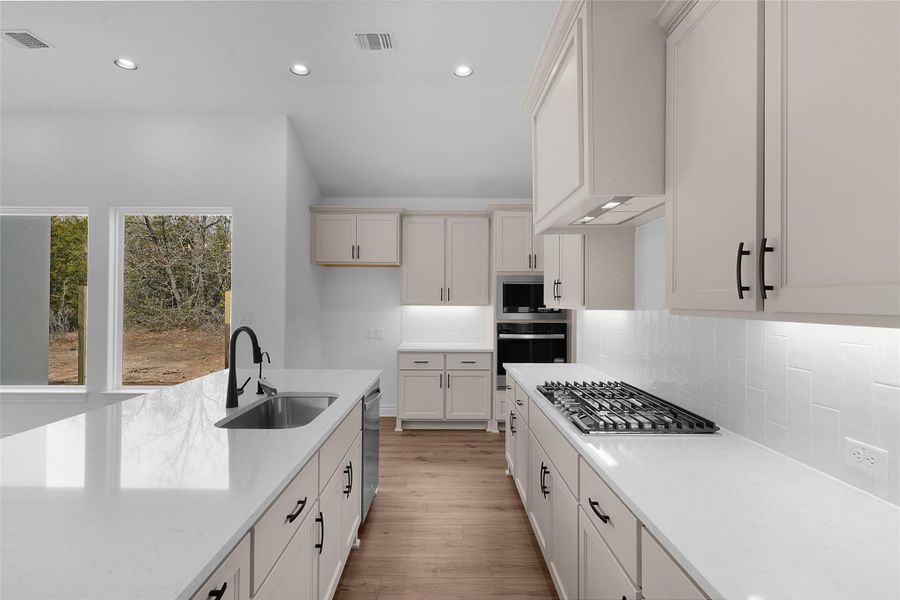 Kitchen with light stone counters, light wood finished floors, recessed lighting, stainless steel appliances, and tasteful backsplash