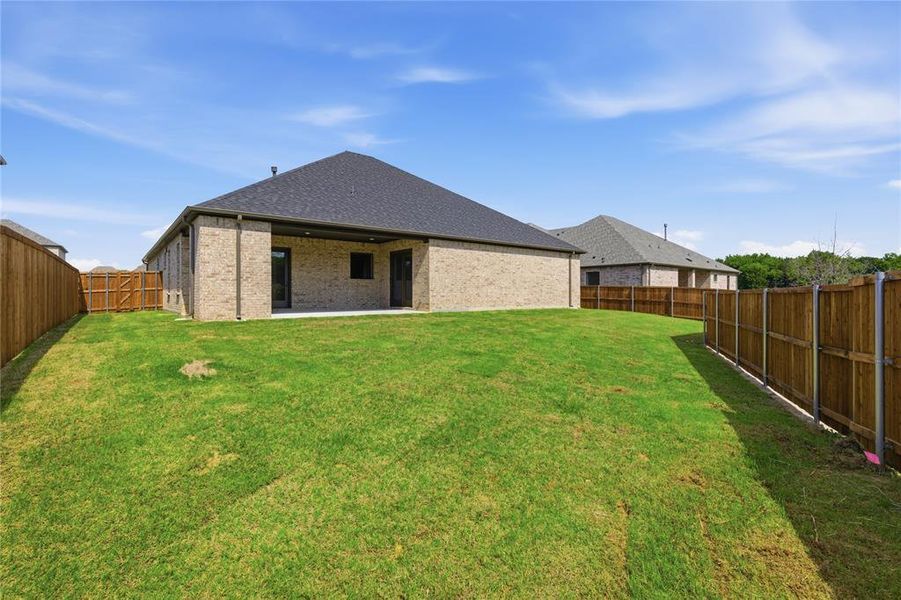 Expansive backyard with a manicured lawn, full privacy fencing, and a covered concrete patio