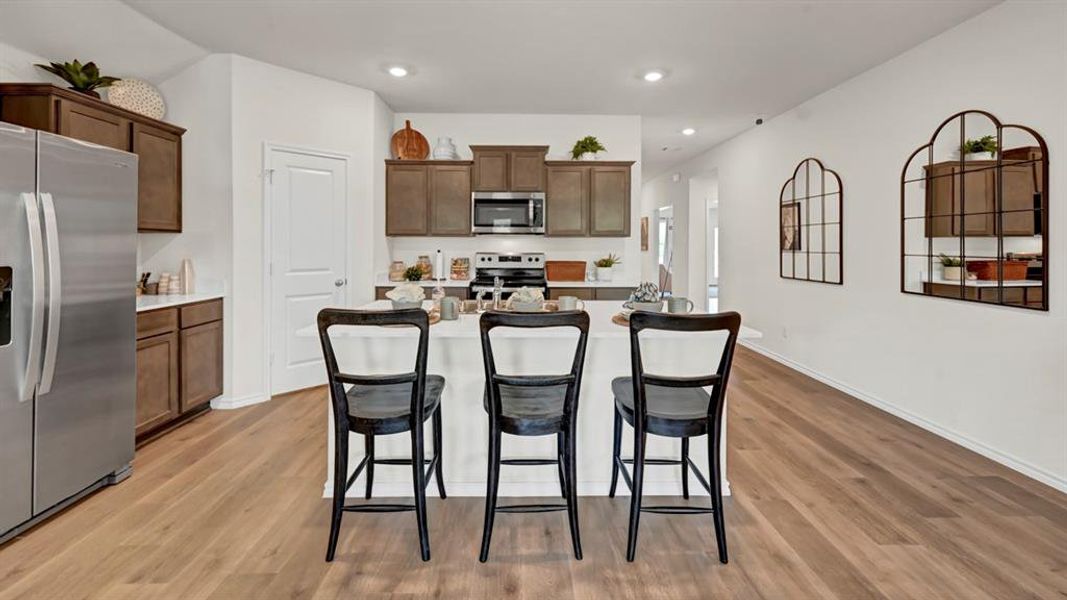 Kitchen with stainless steel appliances, a kitchen breakfast bar, an island with sink, light wood-style flooring, and dark wood finish cabinetry