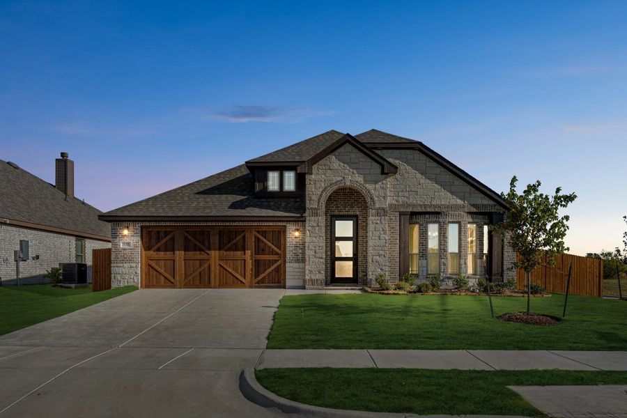 Single-story home with stone and brick exterior, wood garage doors, arched entry, and green front lawn at dusk.