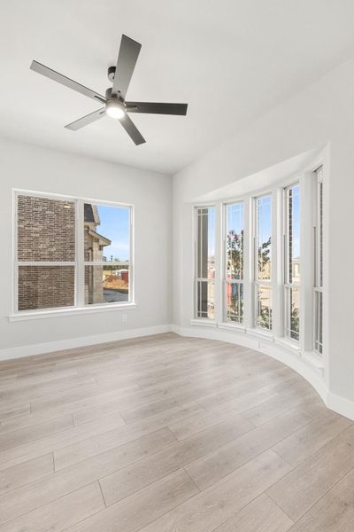 Empty room with light wood floors, ceiling fan, and curved bay window wall
