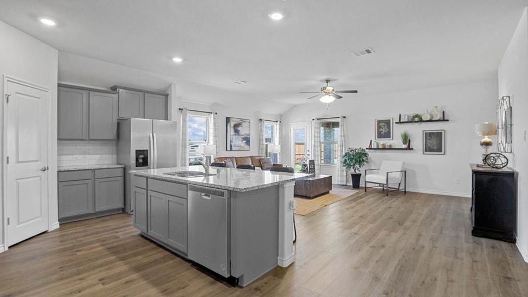 Kitchen featuring light stone countertops, backsplash, an island with sink, appliances with stainless steel finishes, and gray cabinetry