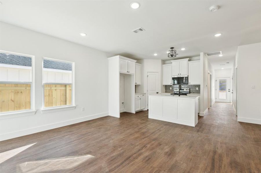 Kitchen with white cabinetry, dark hardwood / wood-style flooring, a center island with sink, and backsplash