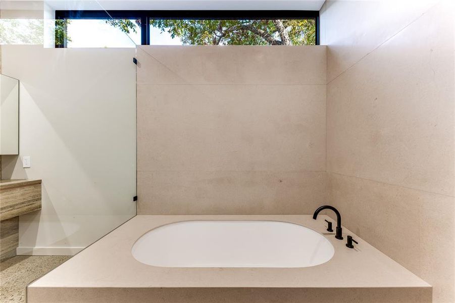 Bathtub with windows providing natural light in primary bathroom.