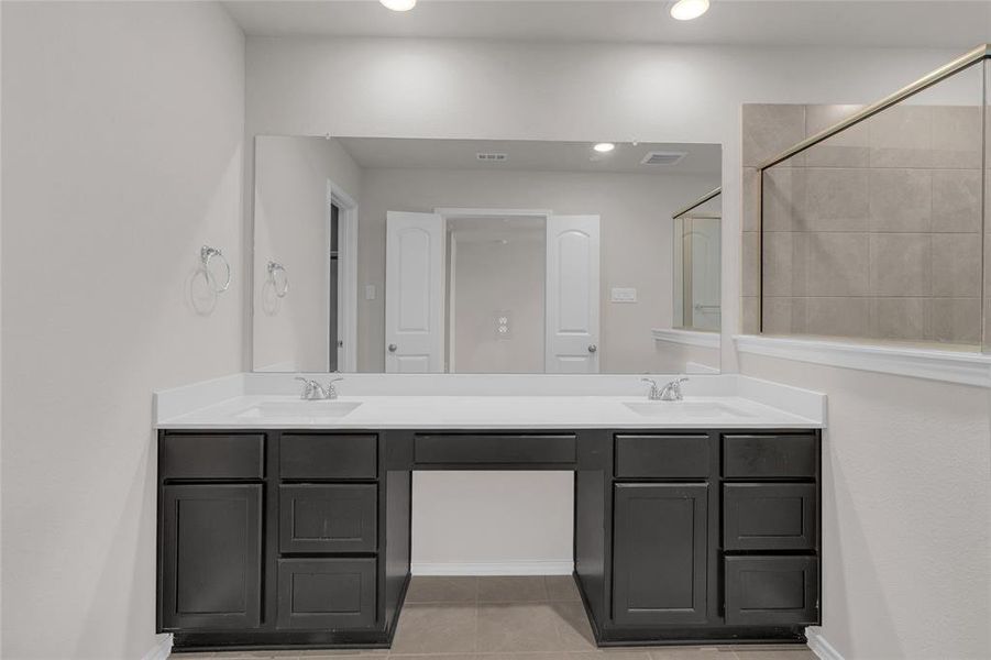 This modern primary bathroom features dual sinks with a spacious vanity and ample under-sink storage, complemented by a large mirror and neutral color tones, offering a clean and sleek look.