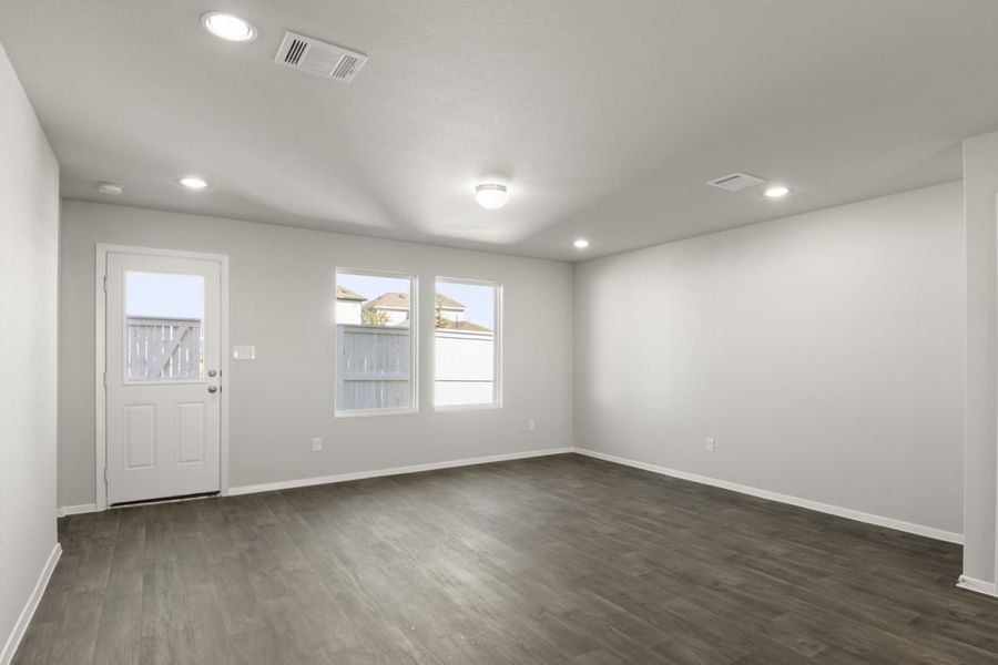 Image of a living room with dark vinyl flooring, light grey walls, two windows and a white back door