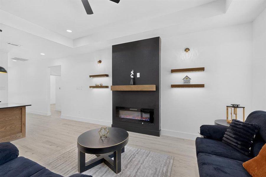 Modern living area featuring a fireplace with a black surround and wood mantel, recessed lighting, wood-finish flooring, and tray ceiling details