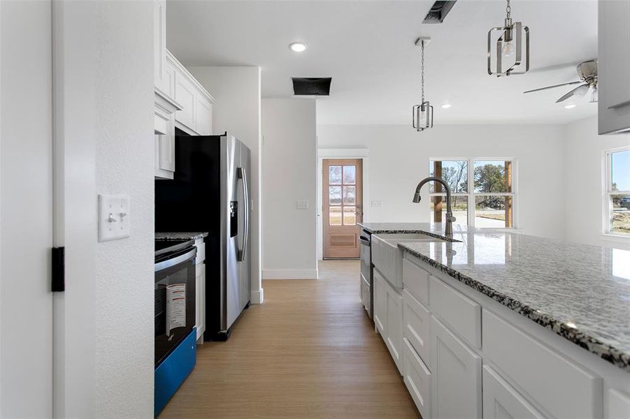 Kitchen with light stone countertops, white cabinetry, ceiling fan, range, and light wood-type flooring