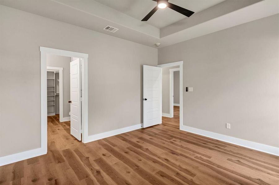 Unfurnished bedroom featuring wood finished floors, a ceiling fan, and a tray ceiling Unfurnished bedroom featuring wood finished floors, a ceiling fan, and a tray ceiling