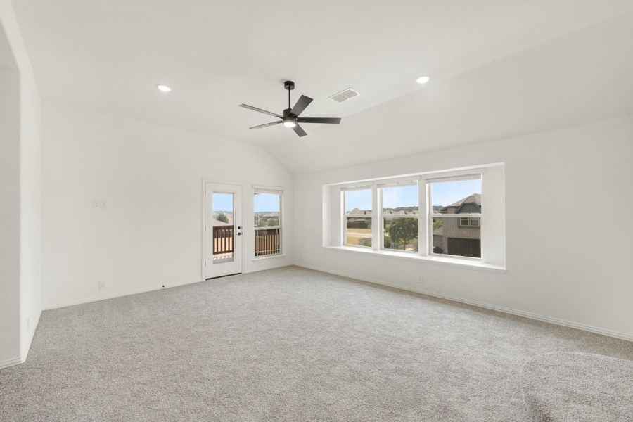 Empty living room with vaulted ceiling, ceiling fan, carpet flooring, and glass door leading to a balcony