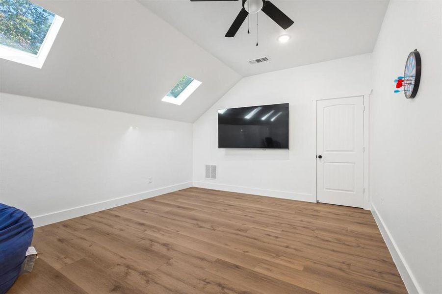 Additional living space with a skylight, lofted ceiling, wood finished floors, and a ceiling fan