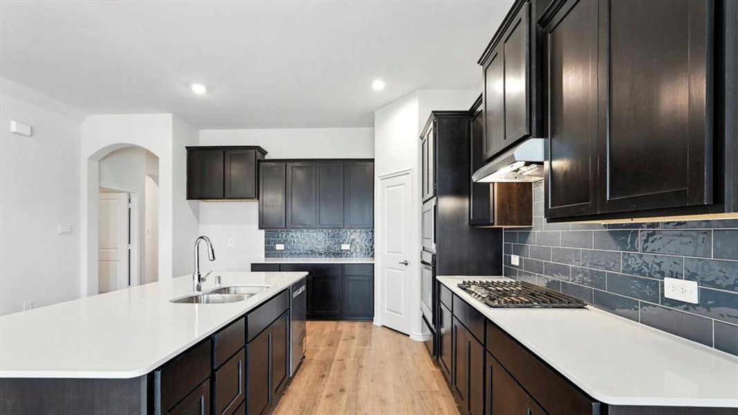 Kitchen featuring light wood-style flooring, a center island with sink, decorative backsplash, light stone counters, and stainless steel appliances