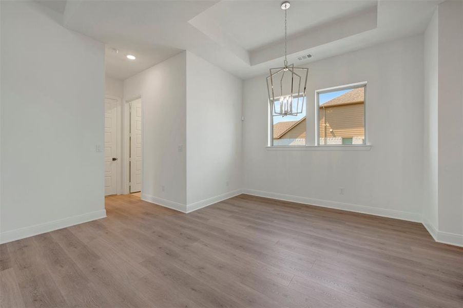 Spacious room featuring wood-finish flooring, a tray ceiling, and a contemporary chandelier