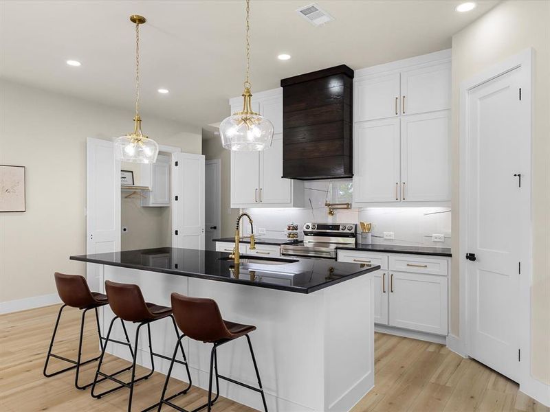 Kitchen island featuring a black countertop, pendant lighting, and light wood-finish flooring