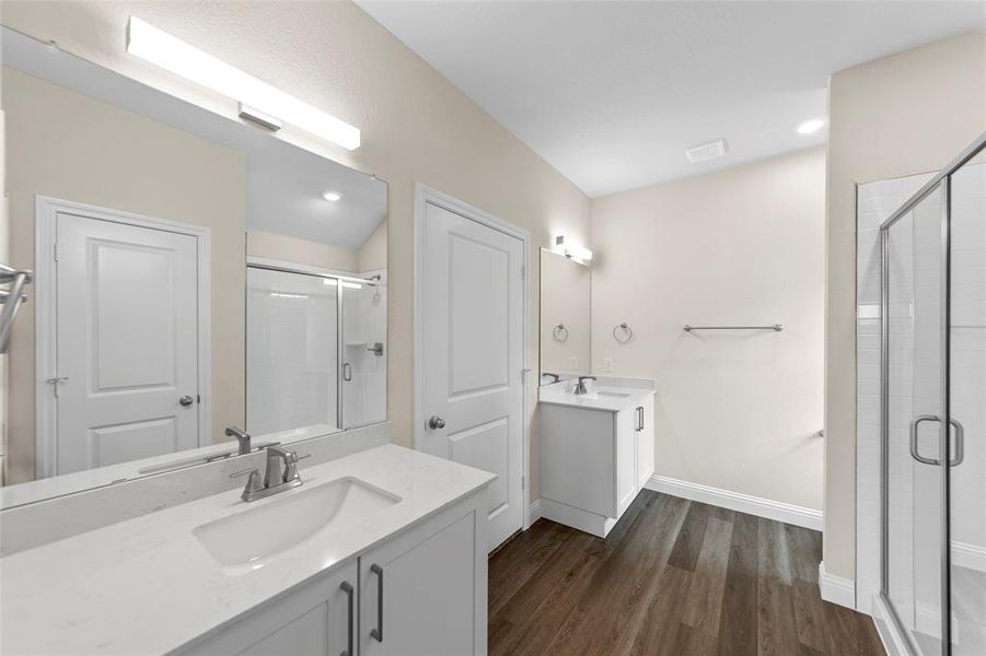 Bathroom featuring dual vanities with white cabinetry and integrated sinks, quartz countertops, a glass-enclosed shower, and wood-finish flooring