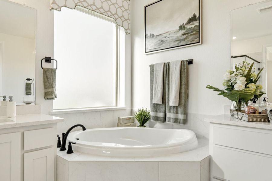 White master bathroom with oval soaking tub, dual vanities, and large window
