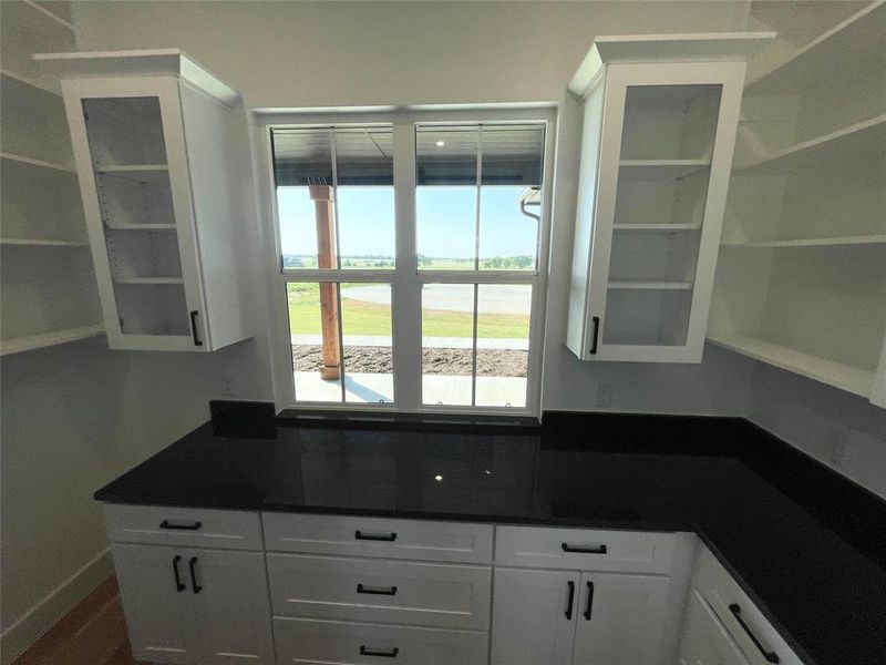 White cabinetry with dark hardware, dark countertops, and a window