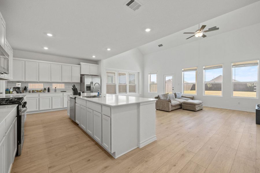 Kitchen featuring white cabinetry, stainless steel appliances, light wood-style flooring, an island with sink, and backsplash