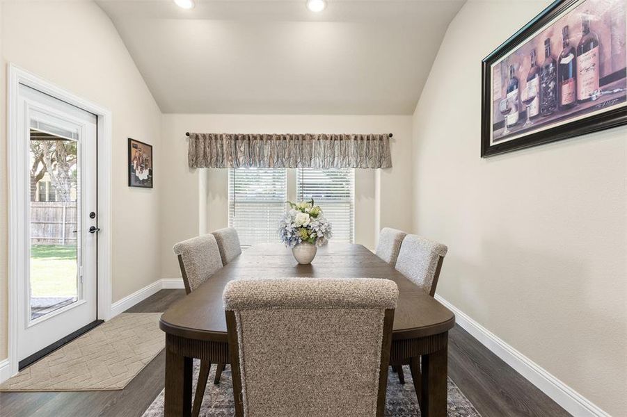 Dining area featuring vaulted ceilings, recessed lighting, wood-finish flooring, a rear exterior door, and a window with blinds Dining area featuring vaulted ceilings, recessed lighting, wood-finish flooring, a rear exterior door, and a window with blinds
