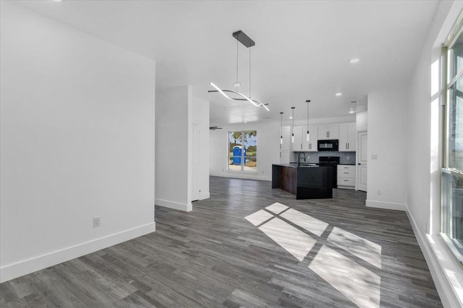 Kitchen featuring dark wood-type flooring, a center island with sink, decorative light fixtures, decorative backsplash, and white cabinets