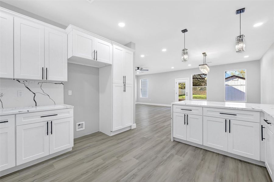 This photo showcases a modern, open-concept kitchen and living area with sleek white cabinetry, marble countertops, and stylish pendant lighting. The space features light wood flooring, ample natural light from large windows, and a seamless flow to the outdoor area, creating a bright and inviting atmosphere perfect for entertaining.