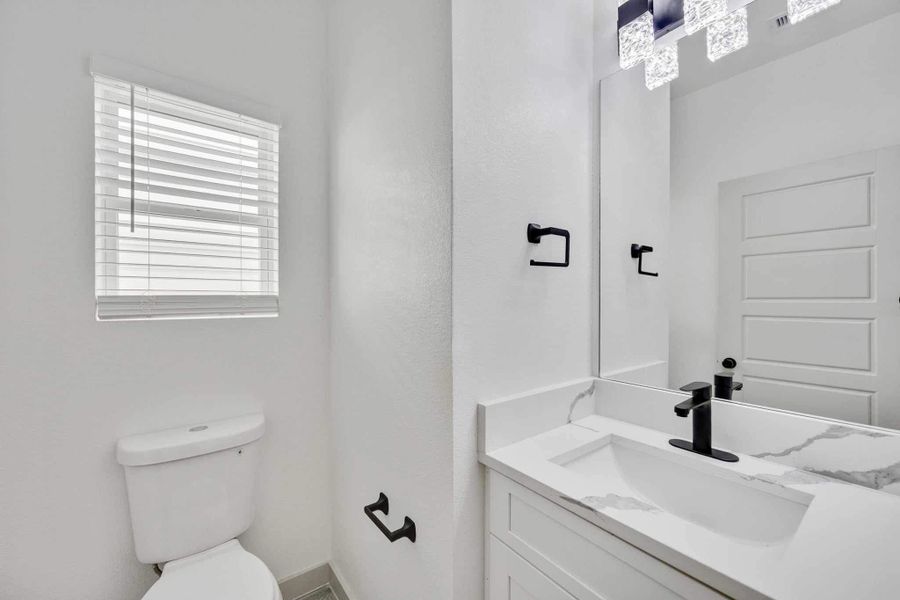 Convenient first-floor half bath with quartz vanity countertop, modern black fixtures, and a large mirror that enhances the space.