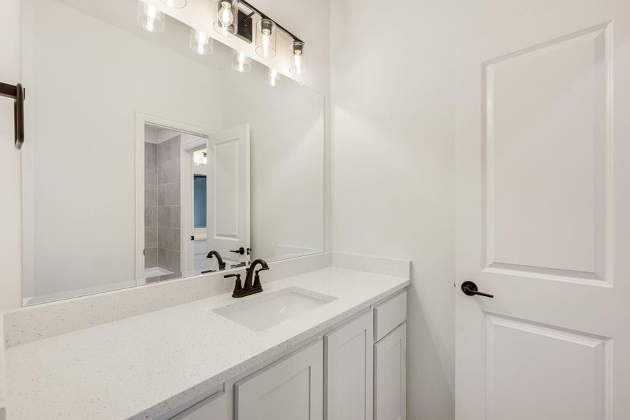 Bathroom vanity with white quartz countertop, undermount sink, dark faucet, and large mirror with modern light bar above.