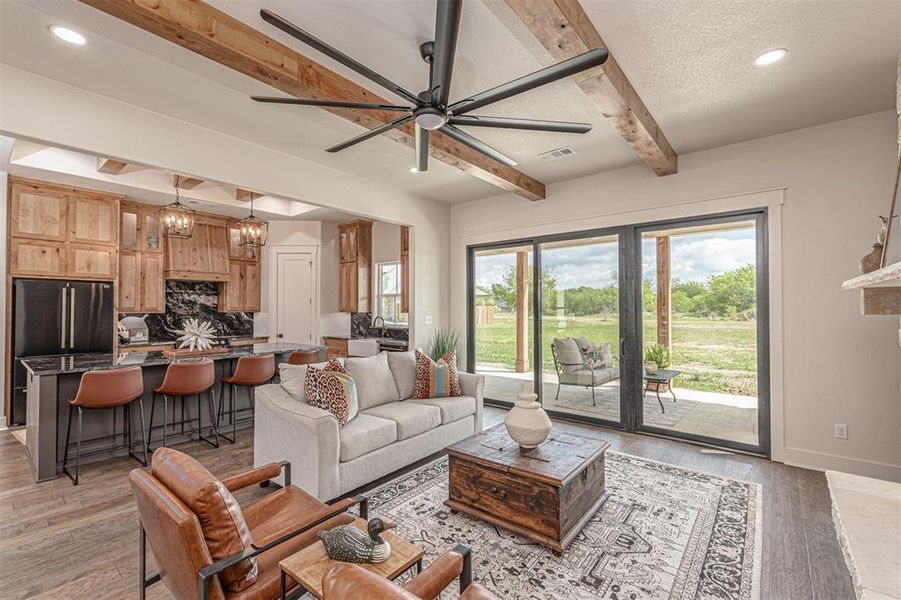 Living area featuring a chandelier, light wood finished floors, a ceiling fan, beamed ceiling, and a textured ceiling